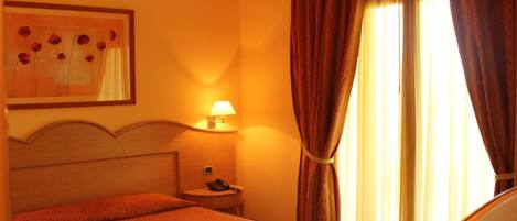 A hotel room with a bed, a nightstand, a lamp, a painting on the wall, and curtains on the window.