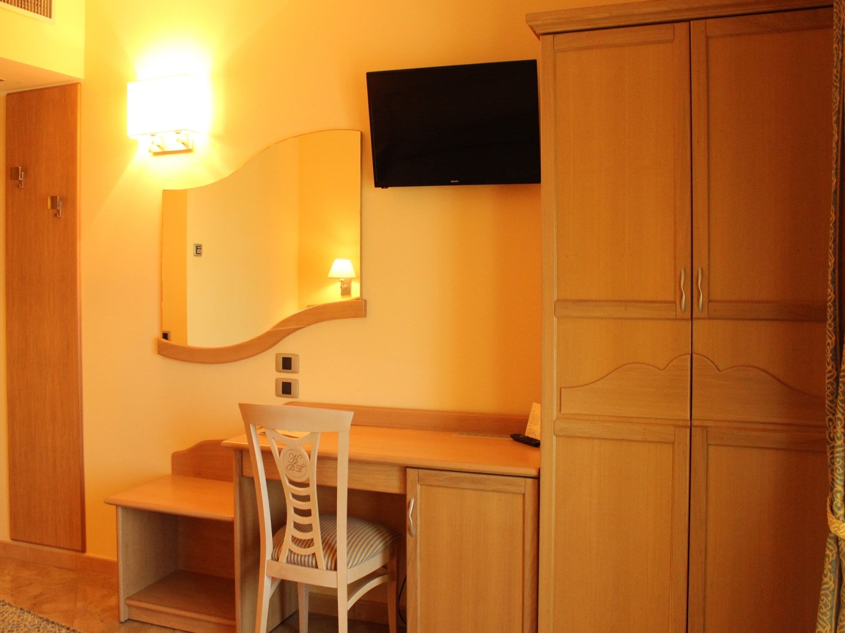 Une chambre d’hôtel avec un bureau en bois, une chaise, un téléviseur à écran plat fixé au mur et une armoire.