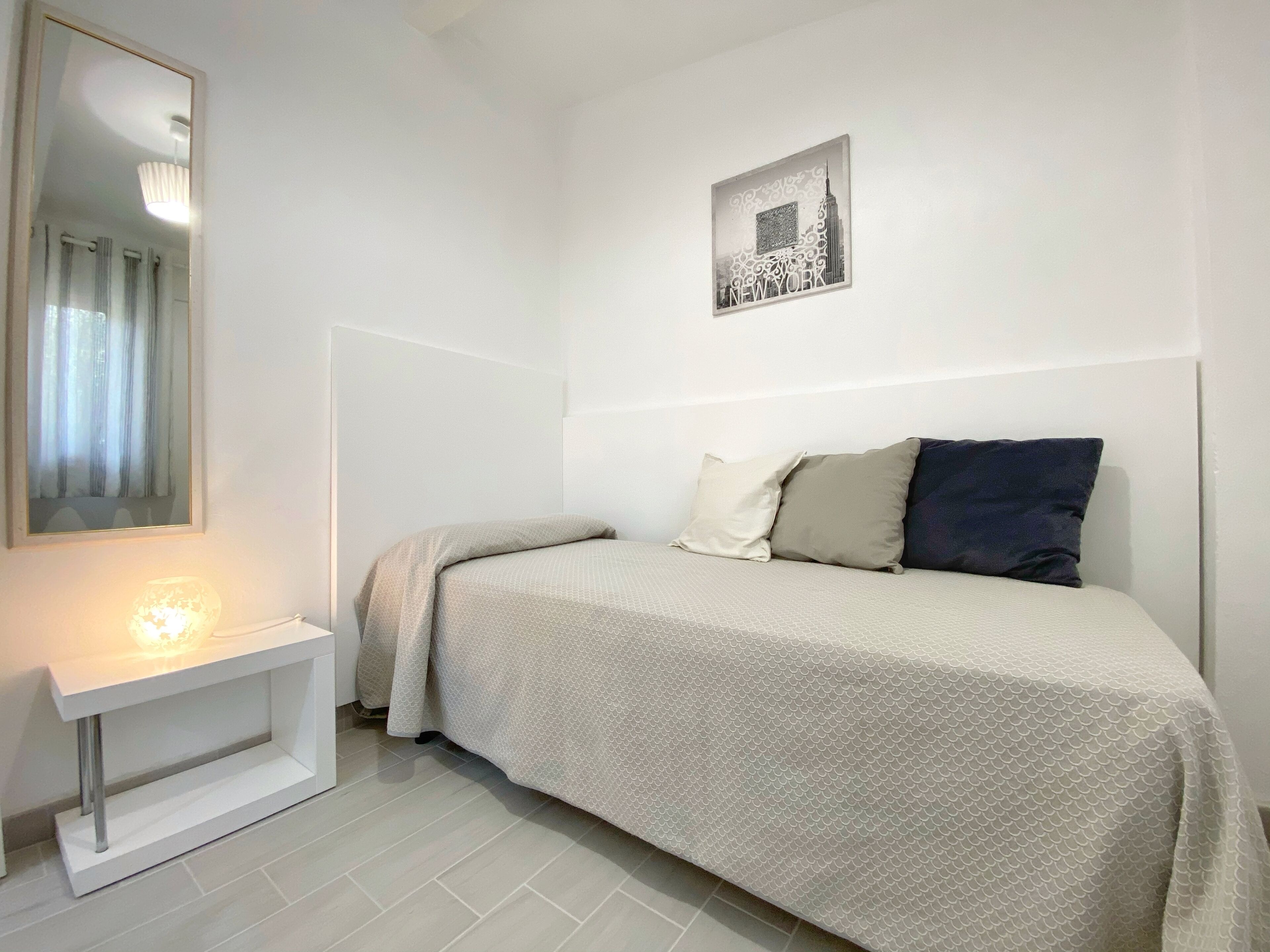 Quarto com cama, mesa de cabeceira com abajur, quadro na parede e espelho.
