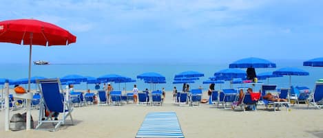 Una playa con sombrillas azules y sillas de descanso.