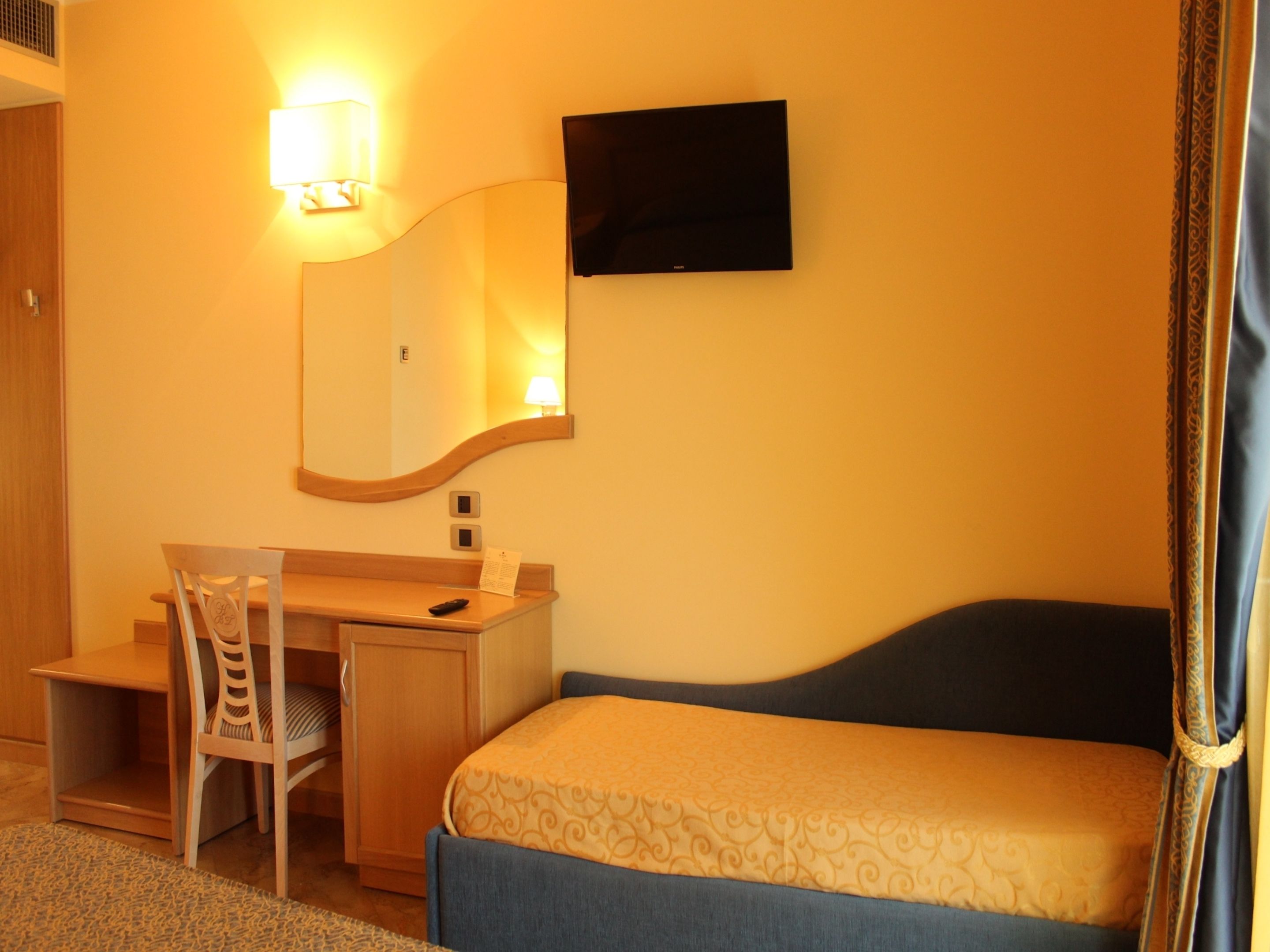 Habitación de hotel con cama, escritorio, silla, televisor de pantalla plana y espejo instalado en la pared.