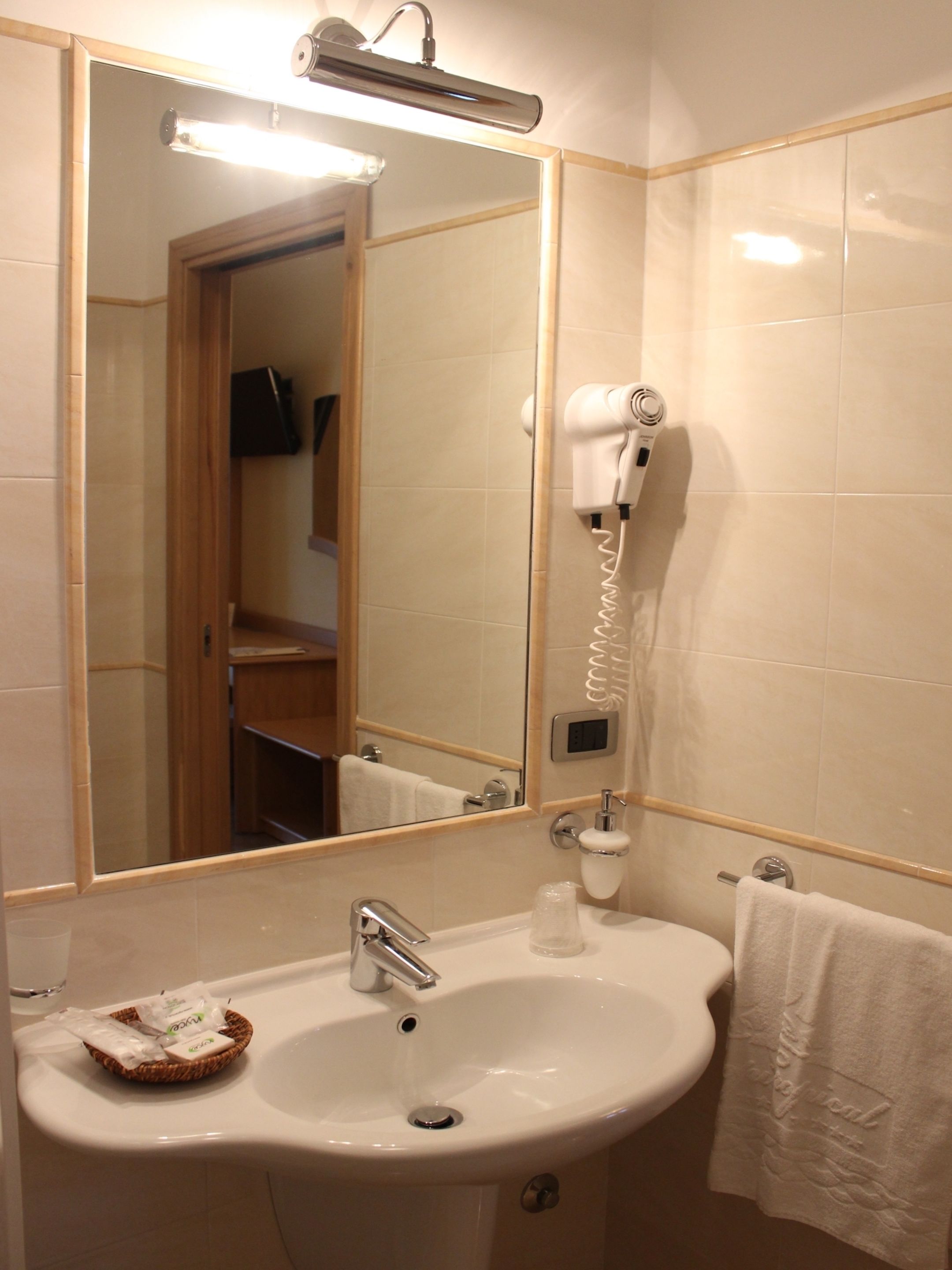Une salle de bain équipée d’un lavabo, d’un miroir, d’un sèche-cheveux et d’un porte-serviettes.