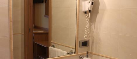 Une salle de bain équipée d’un lavabo, d’un miroir, d’un sèche-cheveux et d’un porte-serviettes.