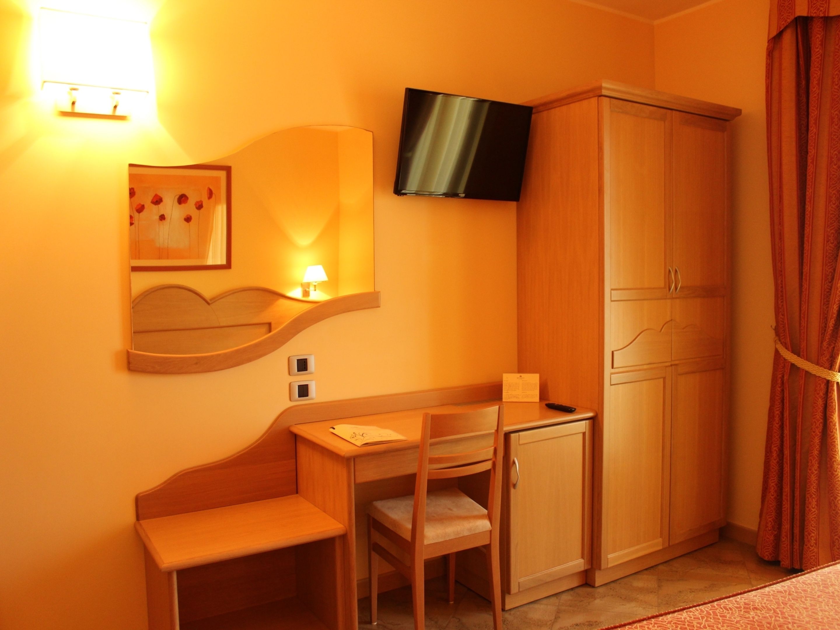 Une chambre d’hôtel équipée d’un bureau, d’une chaise, d’une armoire, d’une télévision et ornée d’un tableau au mur.