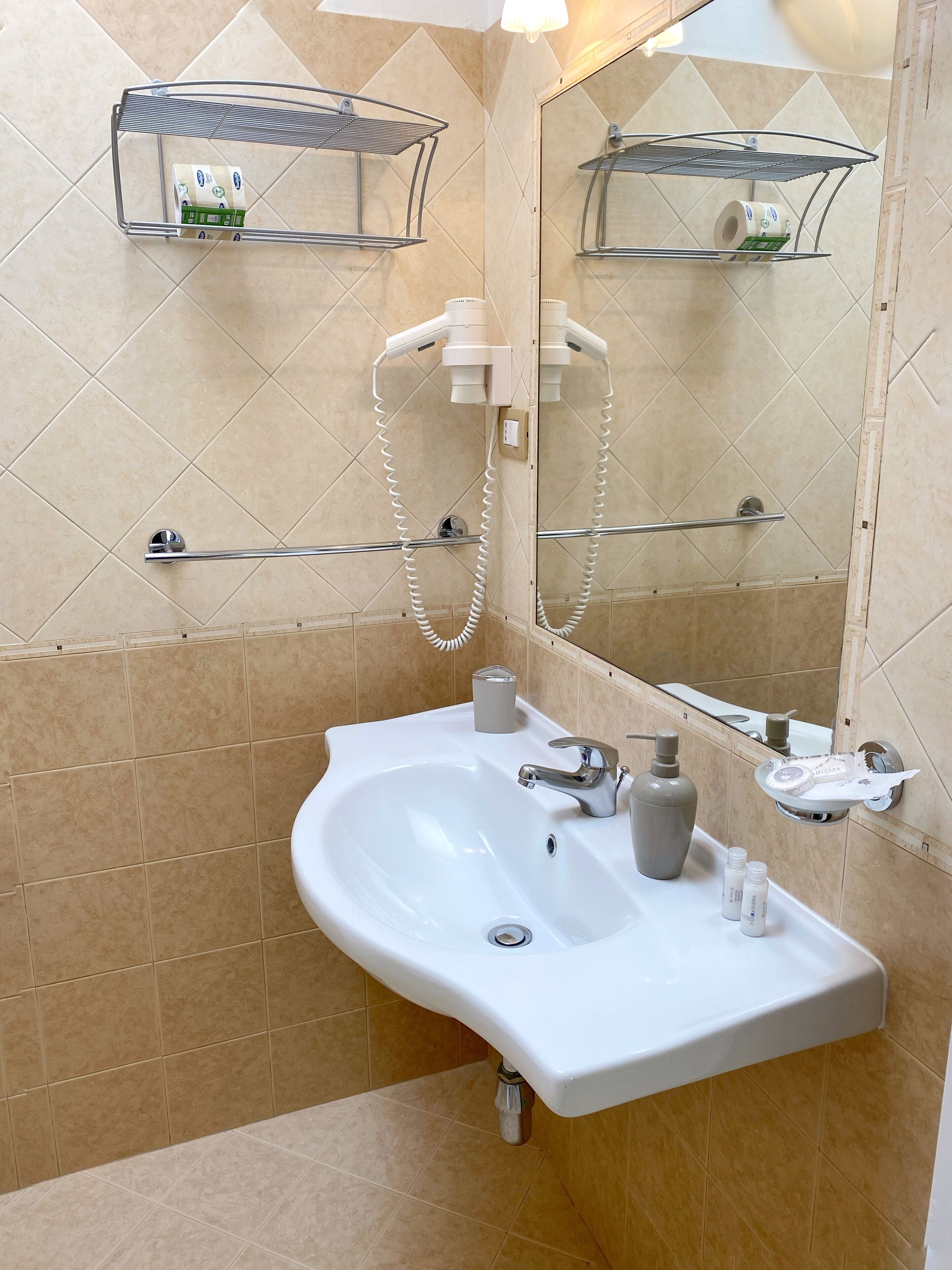A bathroom with a white sink, a mirror, and a shower. There are shelves above the sink and a towel rack.