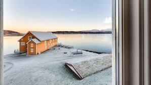 A house with a dock and a boat, overlooking a calm lake with mountains in the background. - Sandtorgholmen Hotel, BW Signature Collection (Harstad)