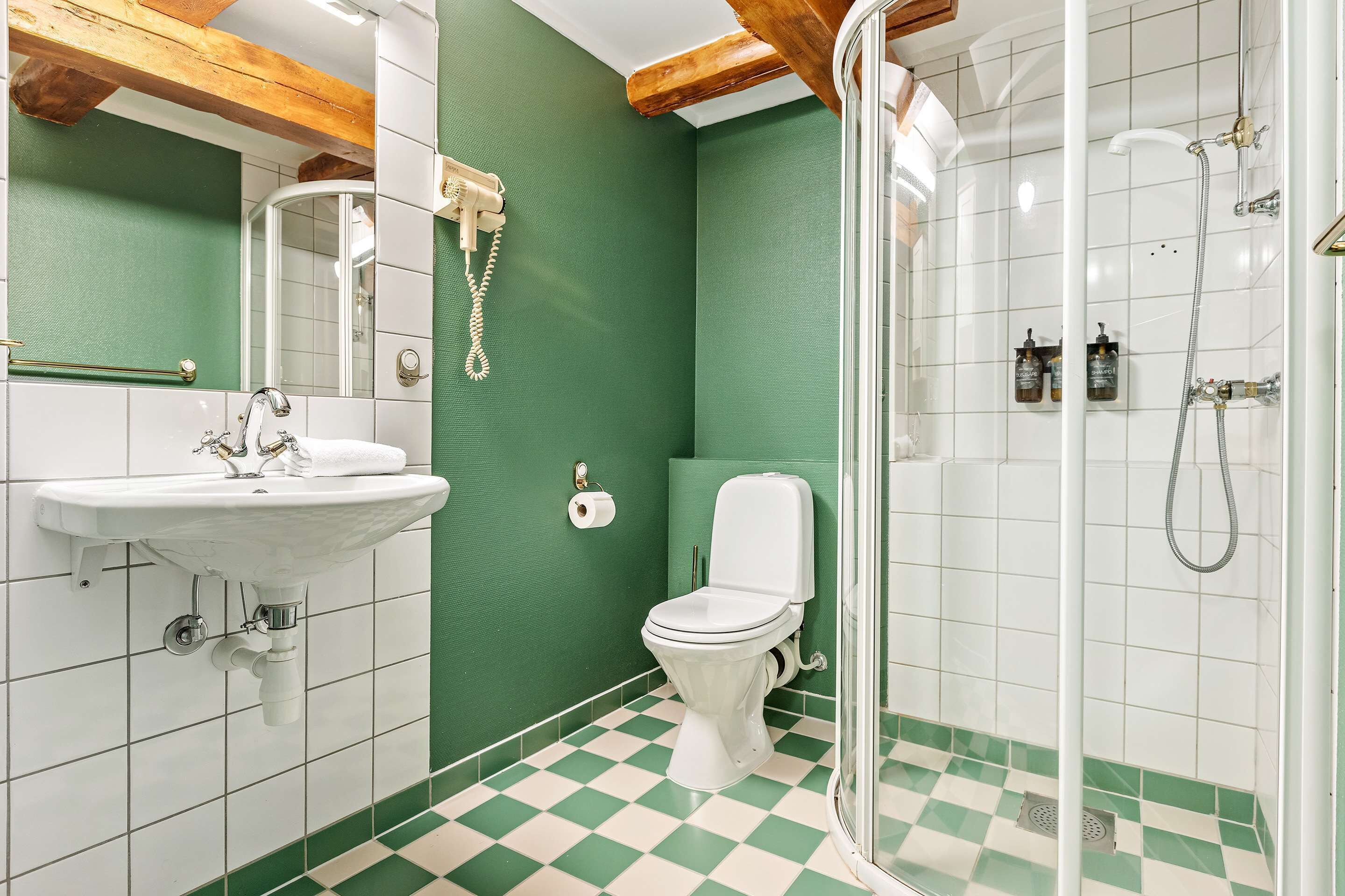 Een badkamer met een wit wastafel, toilet en douche. De muren zijn groen en de vloer heeft een ruitpatroon.