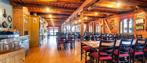 A restaurant with wooden floors and tables, red cushioned chairs, and a wooden ceiling with exposed beams.