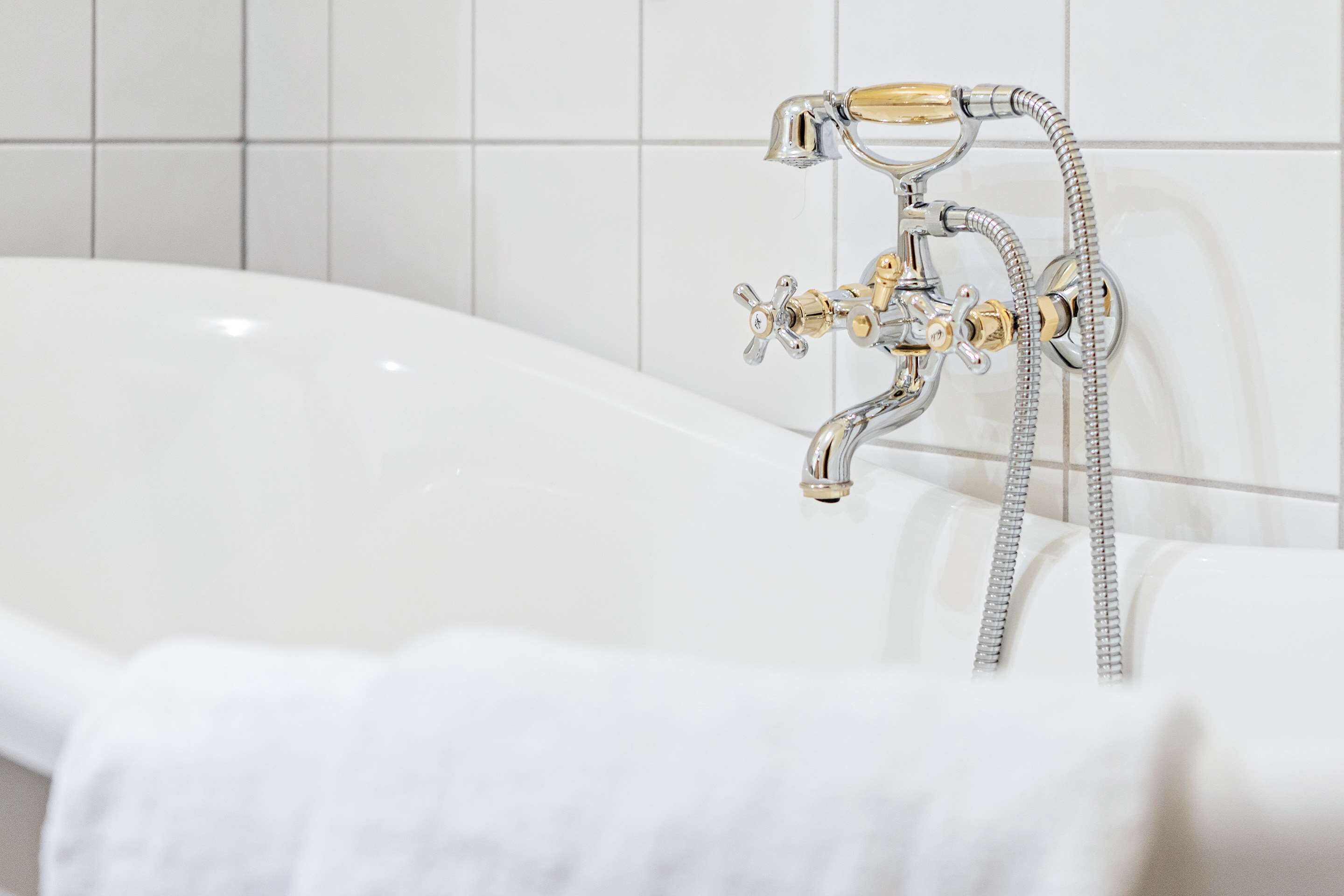 Ein modernes Badezimmer mit einer weißen Badewanne, chromfarbenen Armaturen und einer gefliesten Wand.