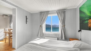 A bedroom with a bed, a window with curtains, a chair, and a view of the sea. - Sandtorgholmen Hotel, BW Signature Collection (Harstad)