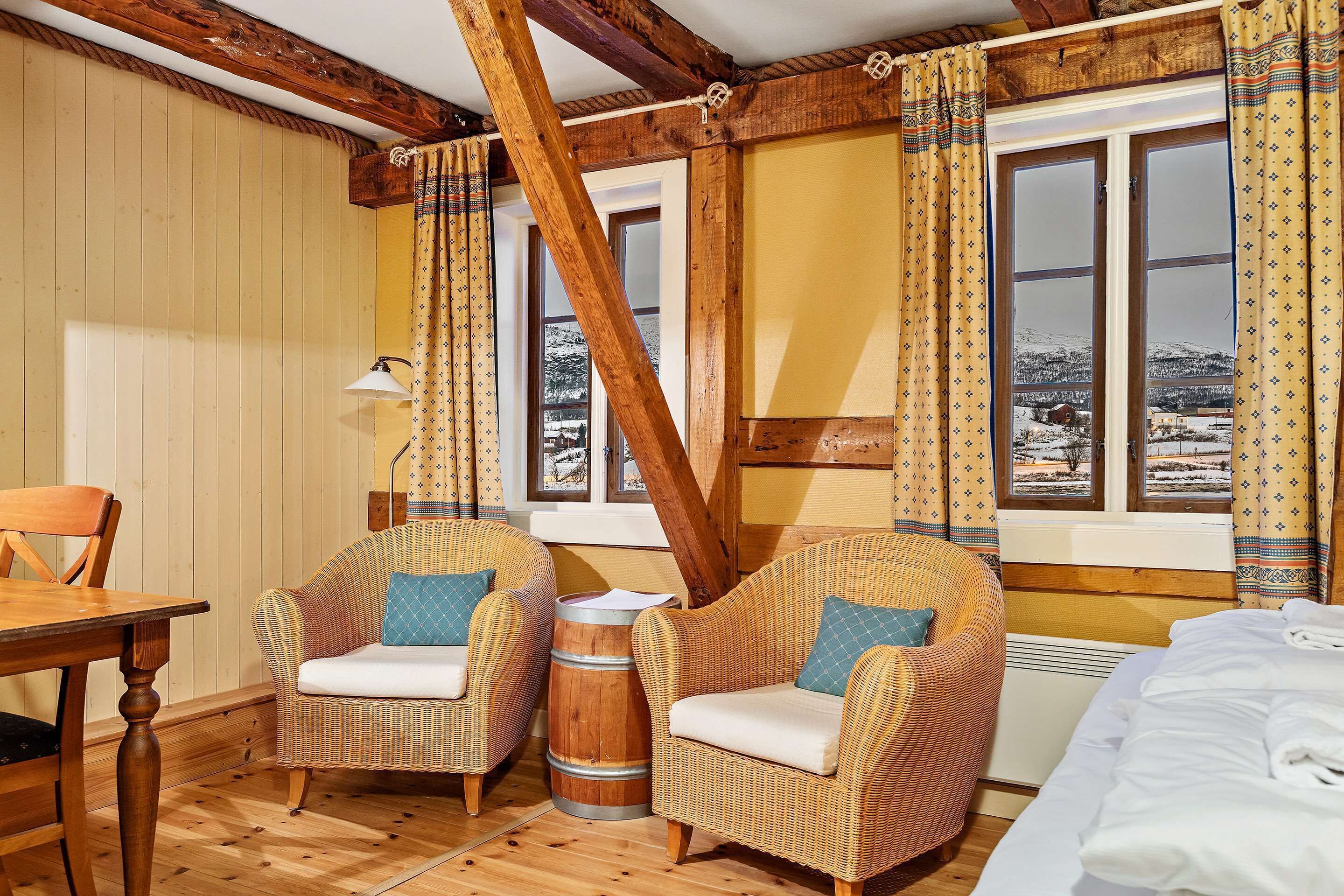 Una habitación acogedora con pisos de madera, dos sillones de mimbre con cojines, una mesa de madera y un barril.