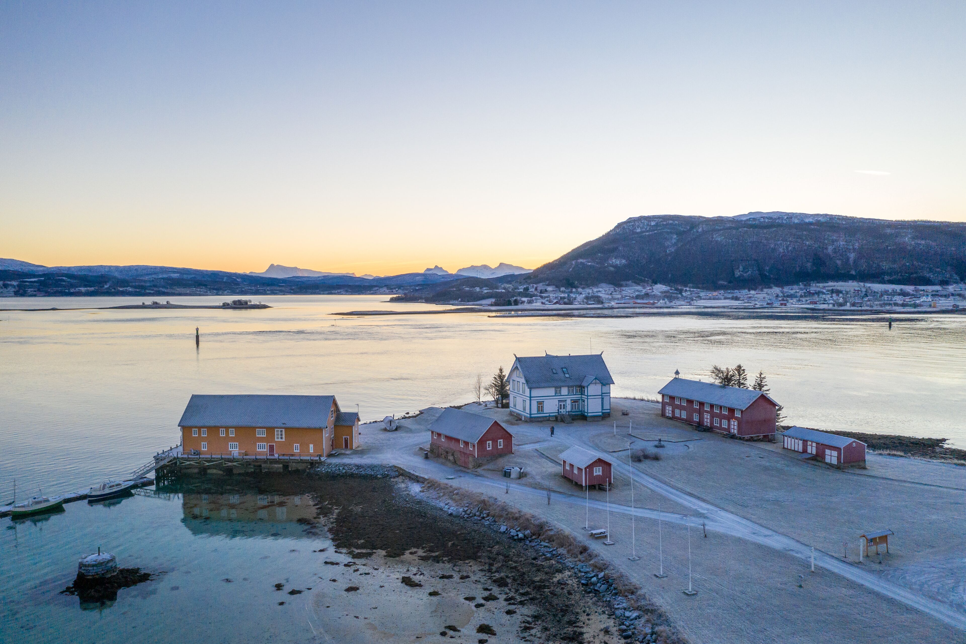 A coastal village with buildings near the water, a dock, and a clear view of the surrounding landscape.