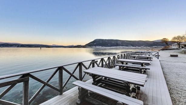 A wooden dock with benches extending over calm water, surrounded by mountains and clear skies. - Sandtorgholmen Hotel, BW Signature Collection (Harstad)