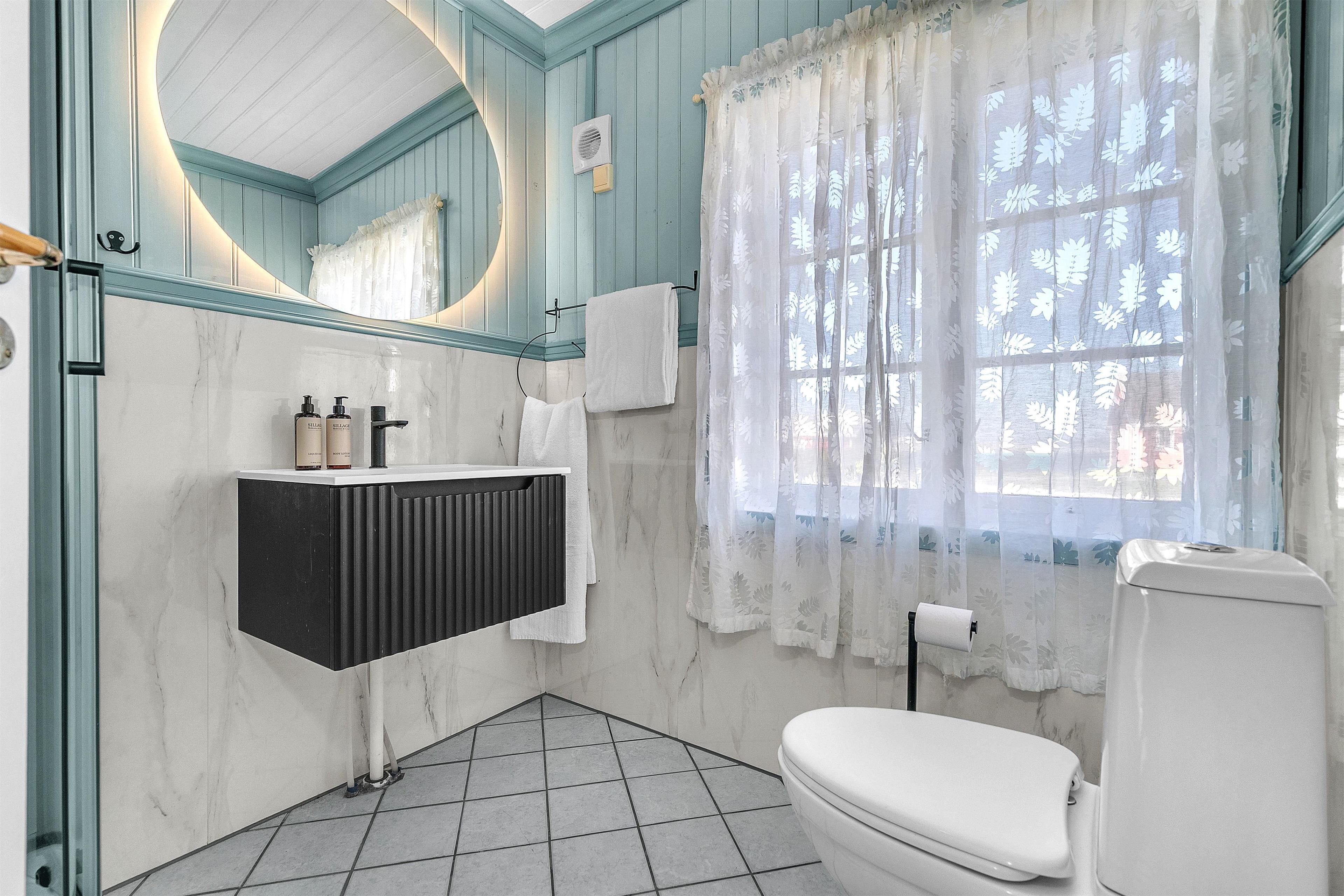 A bathroom with a white toilet, a black radiator, a mirror, and a window with floral curtains.