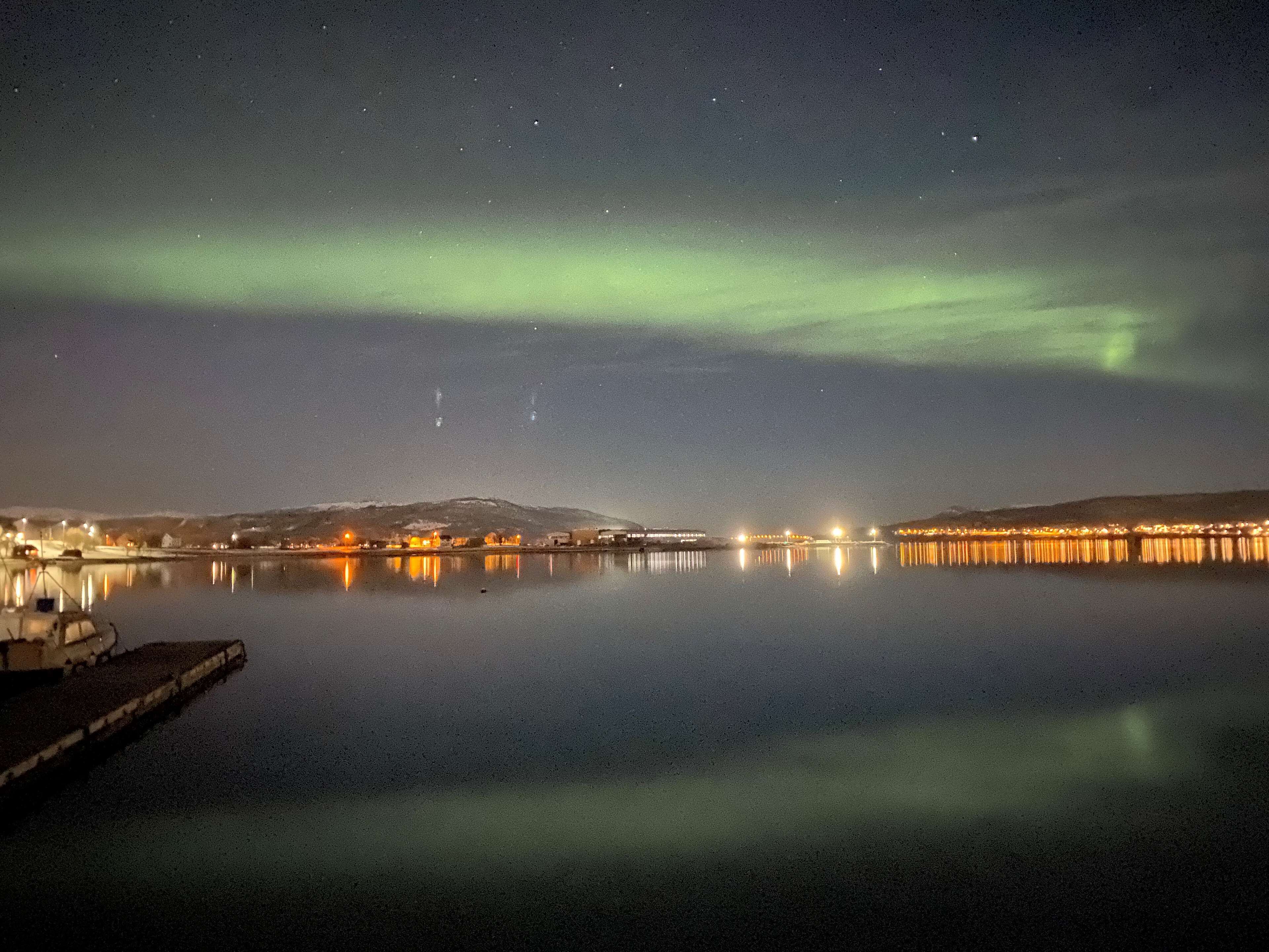 A nighttime view of a calm body of water reflecting lights from a distant shoreline.