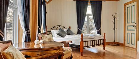 A bedroom with a wooden floor, a four-poster bed, a bedside table, a chair, and a floor lamp.