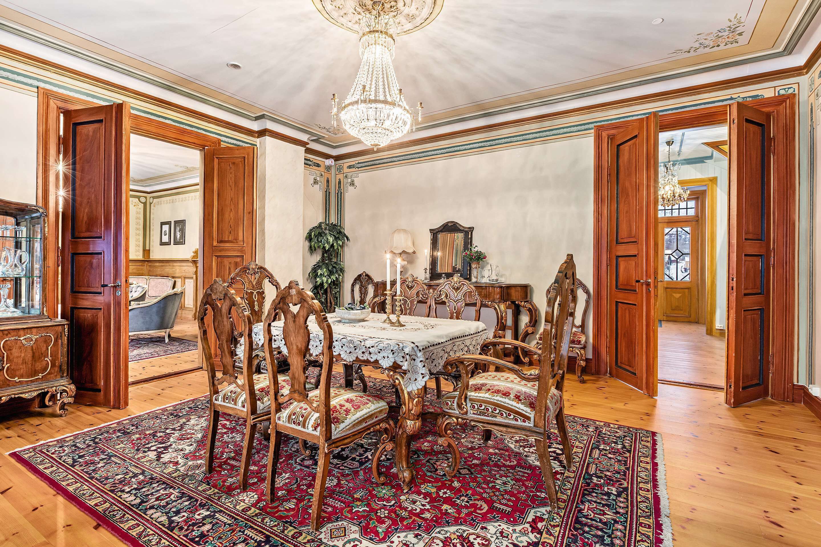 A formal dining room with a chandelier, wooden furniture, and a large rug.