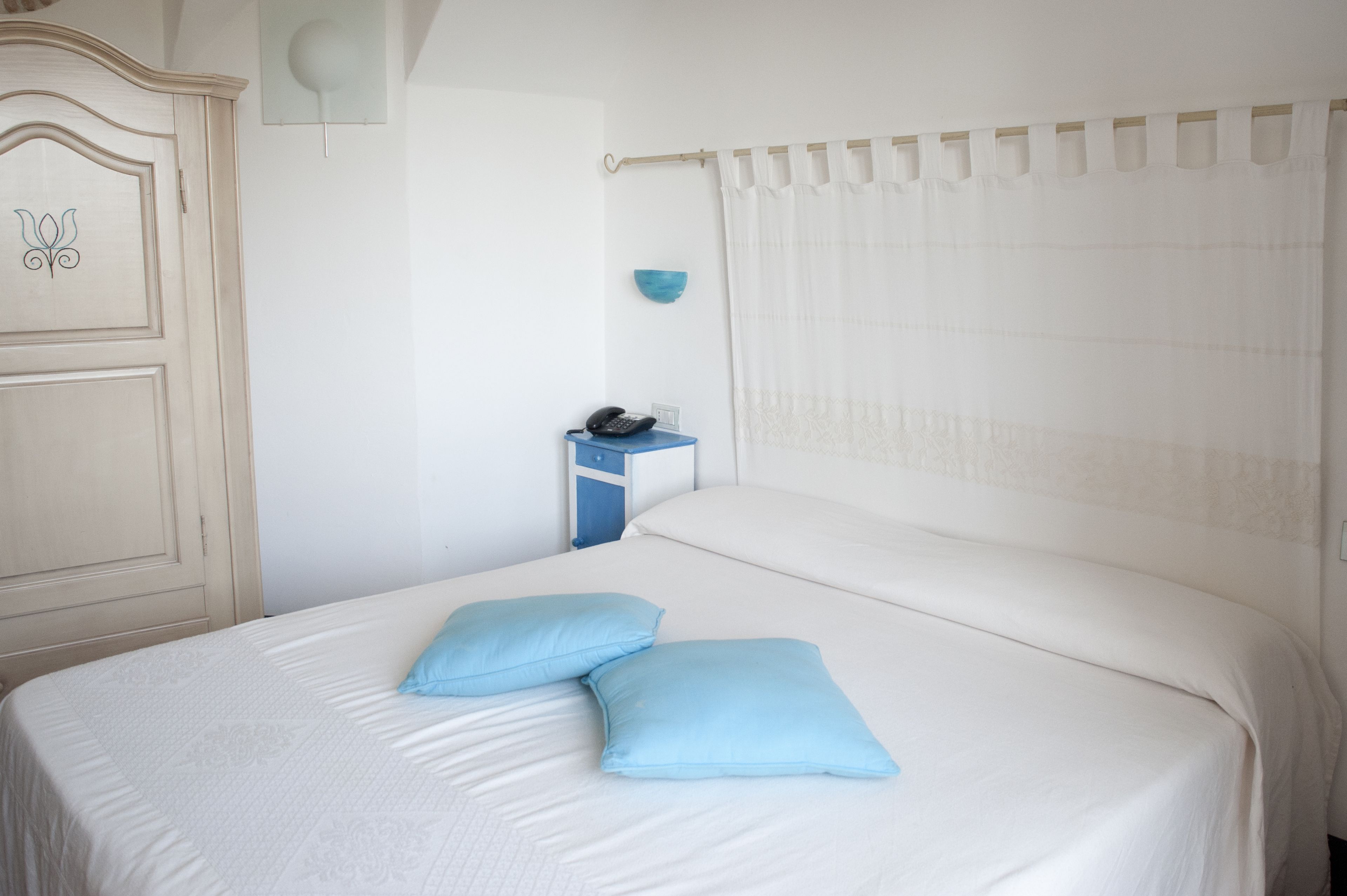 A neatly made bed with two pillows, a bedside table with a phone, and a blue wall decoration.