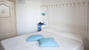 Una cama bien hecha con dos almohadas, una mesita de noche con un teléfono y un adorno azul en la pared.