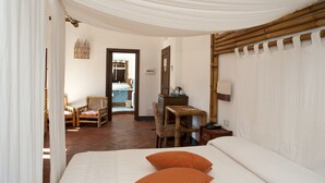 A bedroom with a bed, two chairs, a desk, and a bathroom visible through an open door. - Nascar Hotel (Baunei)