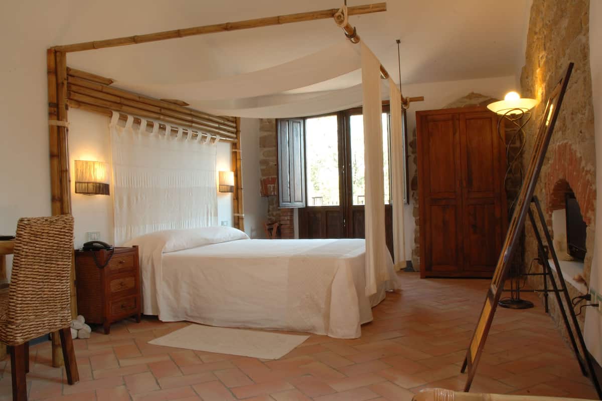 Ein Schlafzimmer mit einem Bett, einem Holzschrank, einem Korbstuhl, einer Lampe und einem Fenster mit Vorhängen.