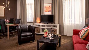 A modern living room with a leather chair, a red sofa, a coffee table, and a TV on a white stand. - Appartementen Valkenburg (Valkenburg aan de Geul)