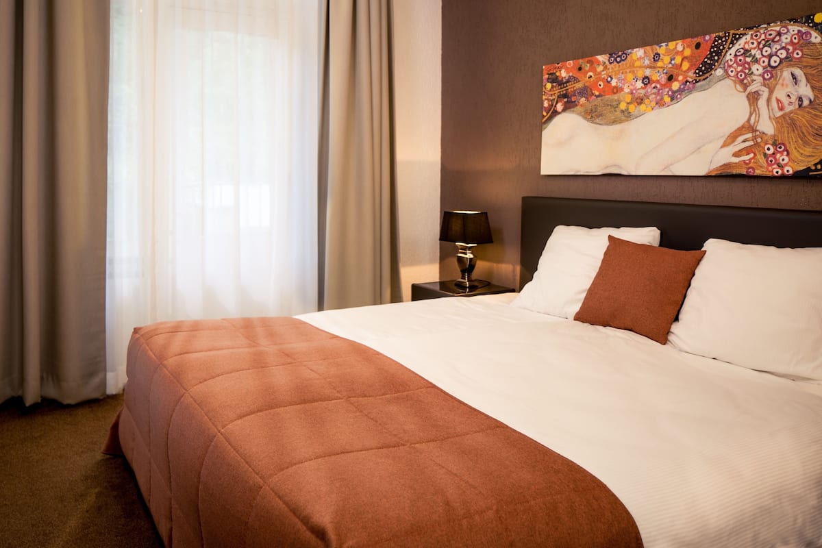 A hotel room with a large bed, a nightstand with a lamp, a vase with flowers, and a painting on the wall.