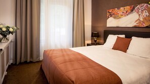 Een hotelkamer met een groot bed, een nachtkastje met een lamp, een vaas met bloemen en een schilderij aan de muur.