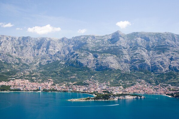 A coastal city with a mountainous backdrop, featuring a harbor and a small island.