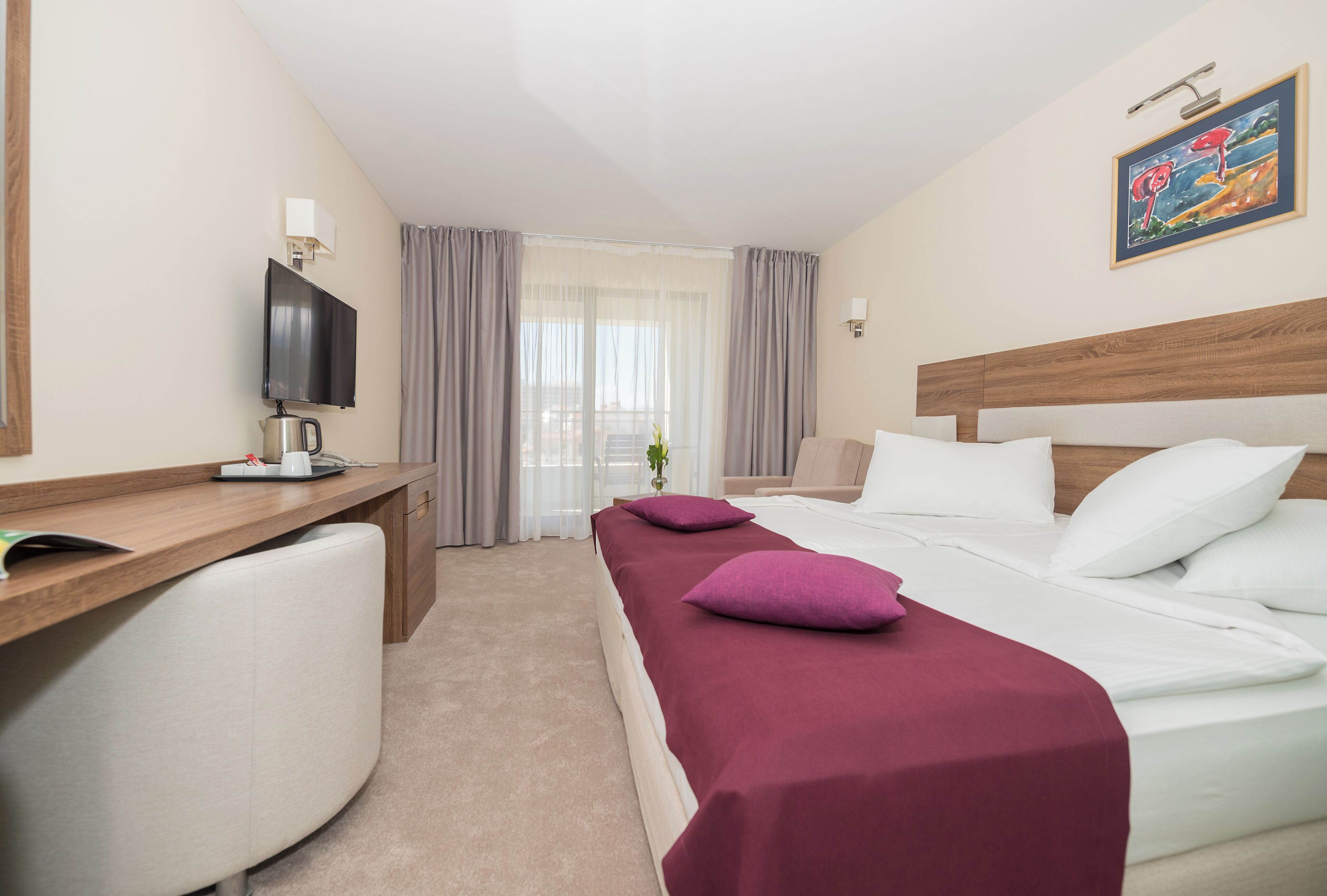 A hotel room with a bed, a desk, a television, and a window with curtains.