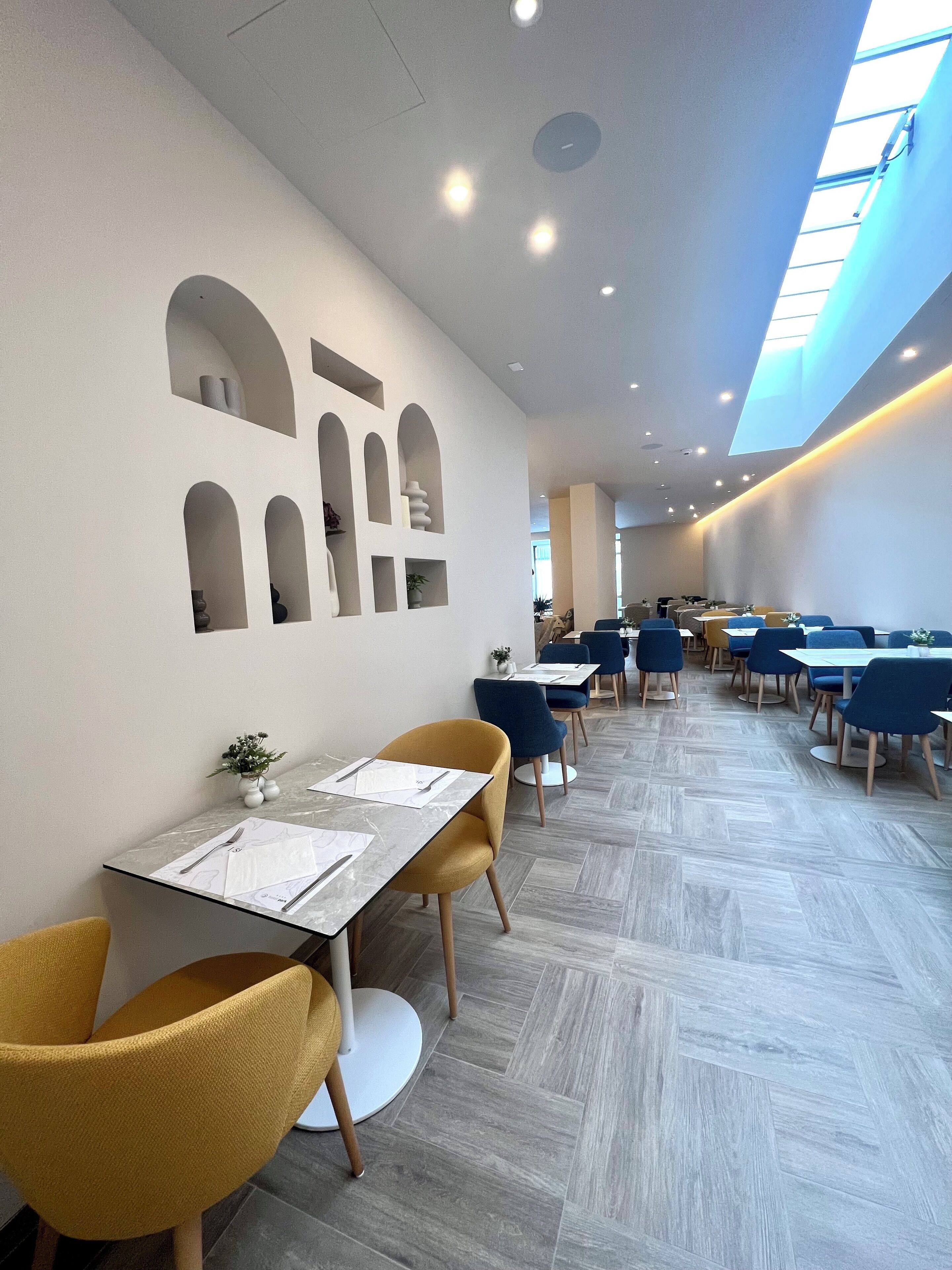 A modern dining area with tables and chairs, recessed lighting, and a skylight.