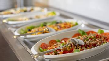 A buffet with various dishes, including a salad with tomatoes, chickpeas, and greens, and a spoon in one of the bowls.