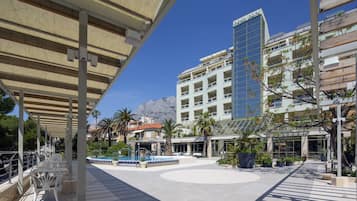 Un hotel de diseño moderno, con fachada de vidrio amplia, piscina y zona exterior cubierta con asientos.