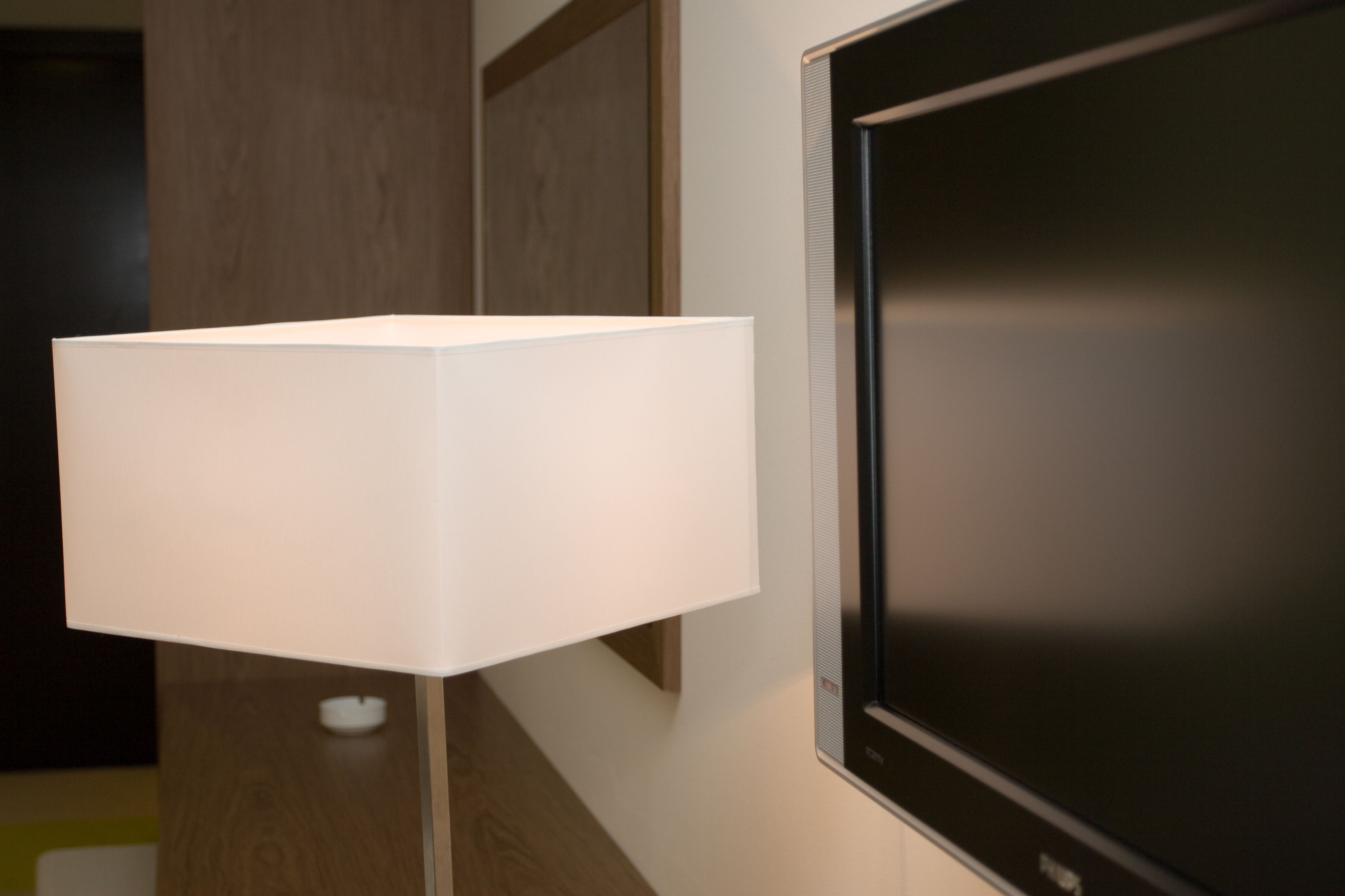 A modern room with a large flat-screen TV mounted on the wall, a white floor lamp, and a wooden door.