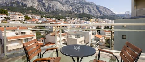 Un balcon avec une table ronde et quatre chaises en bois, d’où l’on a vue sur une ville, avec des bâtiments et des montagnes en arrière-plan.