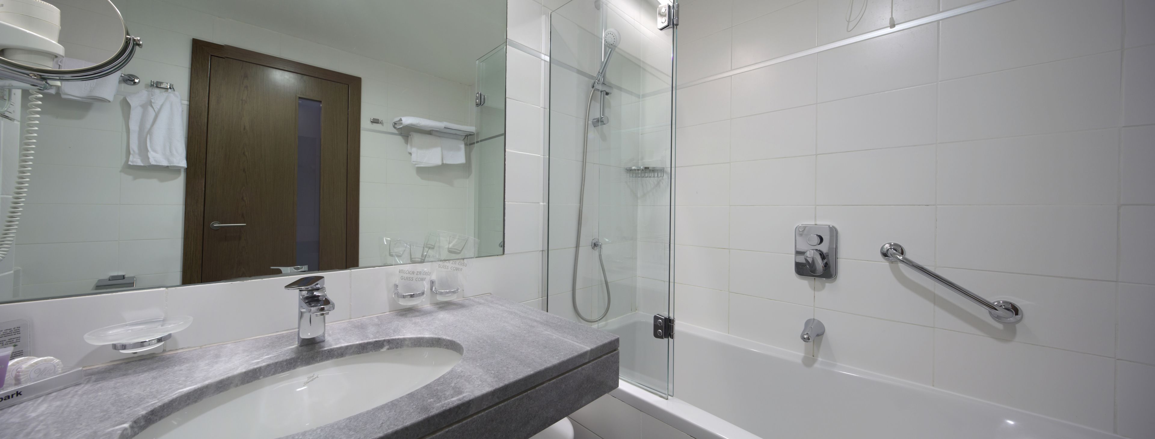 A modern bathroom with a large mirror, a sink, a shower, and a glass-enclosed shower area.