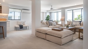 Ein geräumiges Wohnzimmer mit einem großen, beige farbenen Sofa, einem Couchtisch und einem Essbereich mit einem Barhocker.
