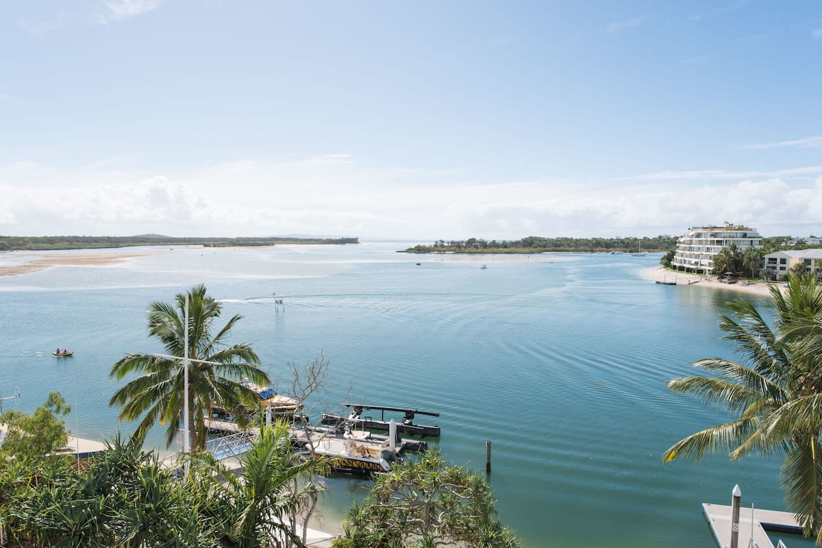 Vista costera con un puerto deportivo, palmeras y un edificio con varios balcones.