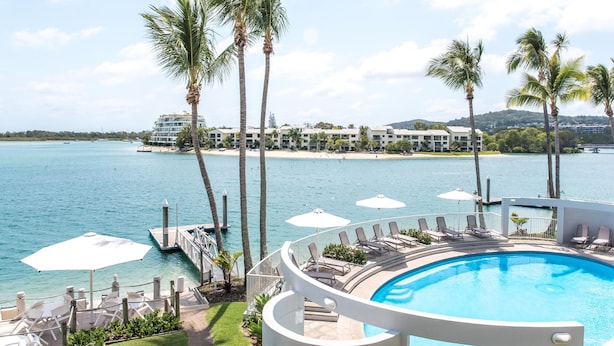 Ein Poolbereich mit Liegestühlen und Sonnenschirmen, mit Blick auf ein Gewässer und ein Strandhotel.