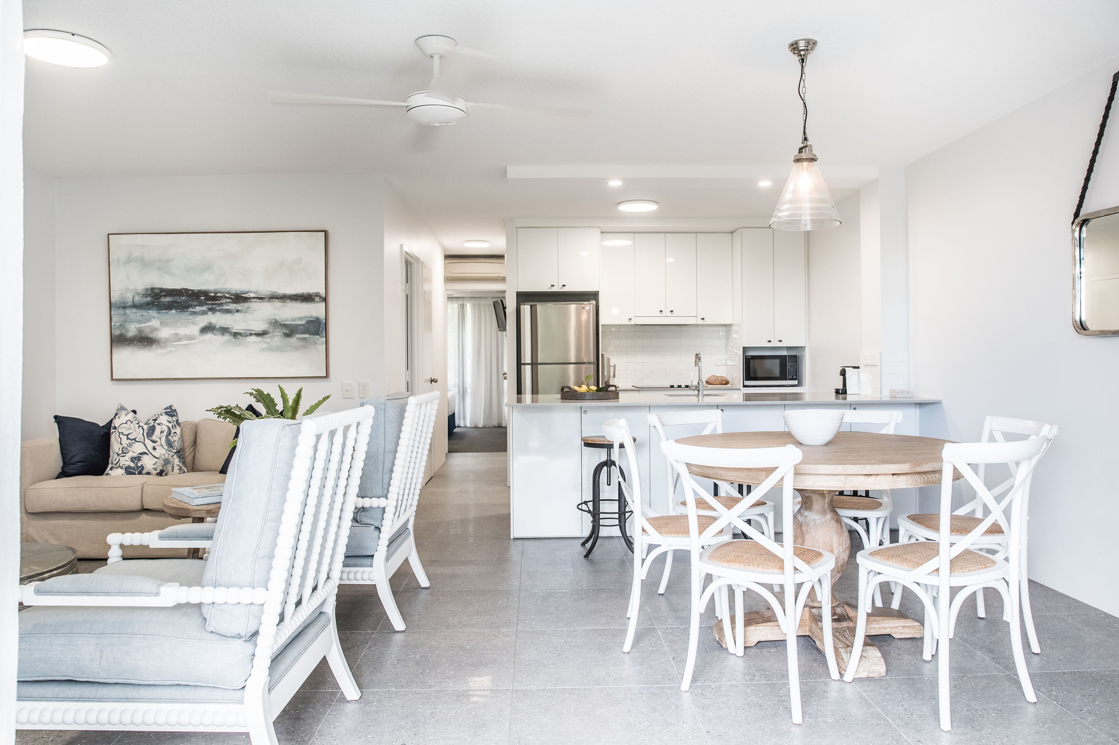 A modern kitchen with white cabinetry, a central island, and a dining area with white chairs.