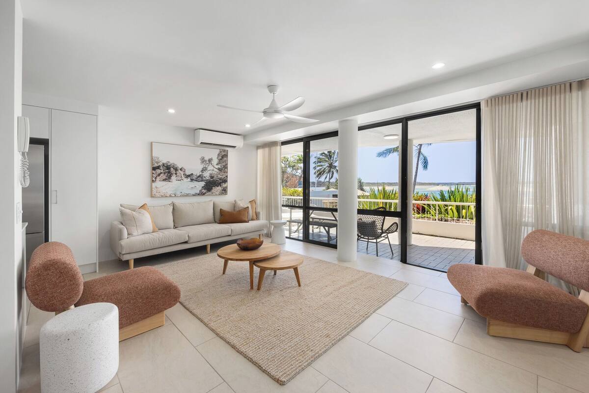 Una sala de estar moderna con un sofá, dos sillones, una mesa de centro y un ventanal con vista a la playa.