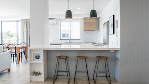 Eine moderne Küche mit weißer Arbeitsplatte, drei Barhocker, Pendelleuchten und einem Holzkorpus.