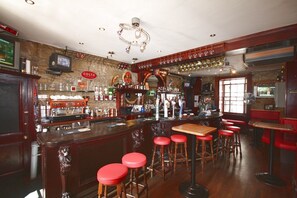 Un bar avec un mur en pierre, un comptoir en bois, des tabourets rouges et un téléviseur.
