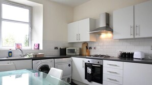 A compact kitchen with white cabinets, a glass table, a microwave, a stove, and a washing machine. - Orchard Hotel (Falkirk)