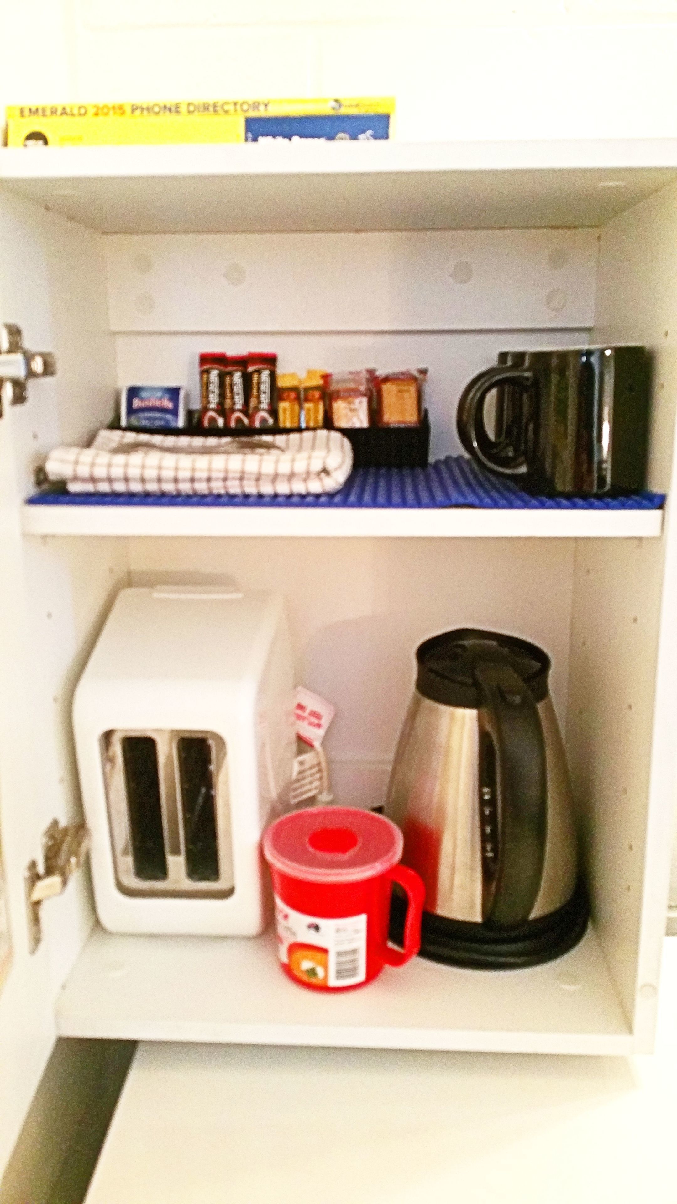 A kitchen with a toaster, a red mug, a coffee pot, and various condiments on shelves.