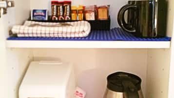 A kitchen with a toaster, a red mug, a coffee pot, and various condiments on shelves.