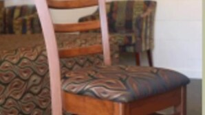 A wooden chair with a patterned cushion in a room with patterned carpet and a table with a colorful tablecloth. - A & A Lodge Motel Emerald (Emerald)