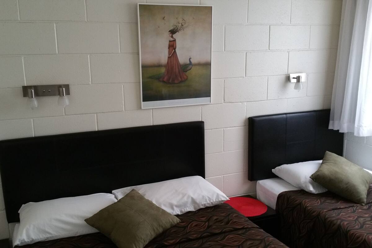 Habitación de hotel con dos camas, cada una con cabecero negro, almohadas blancas y marrones, y una obra de arte enmarcada sobre las camas.