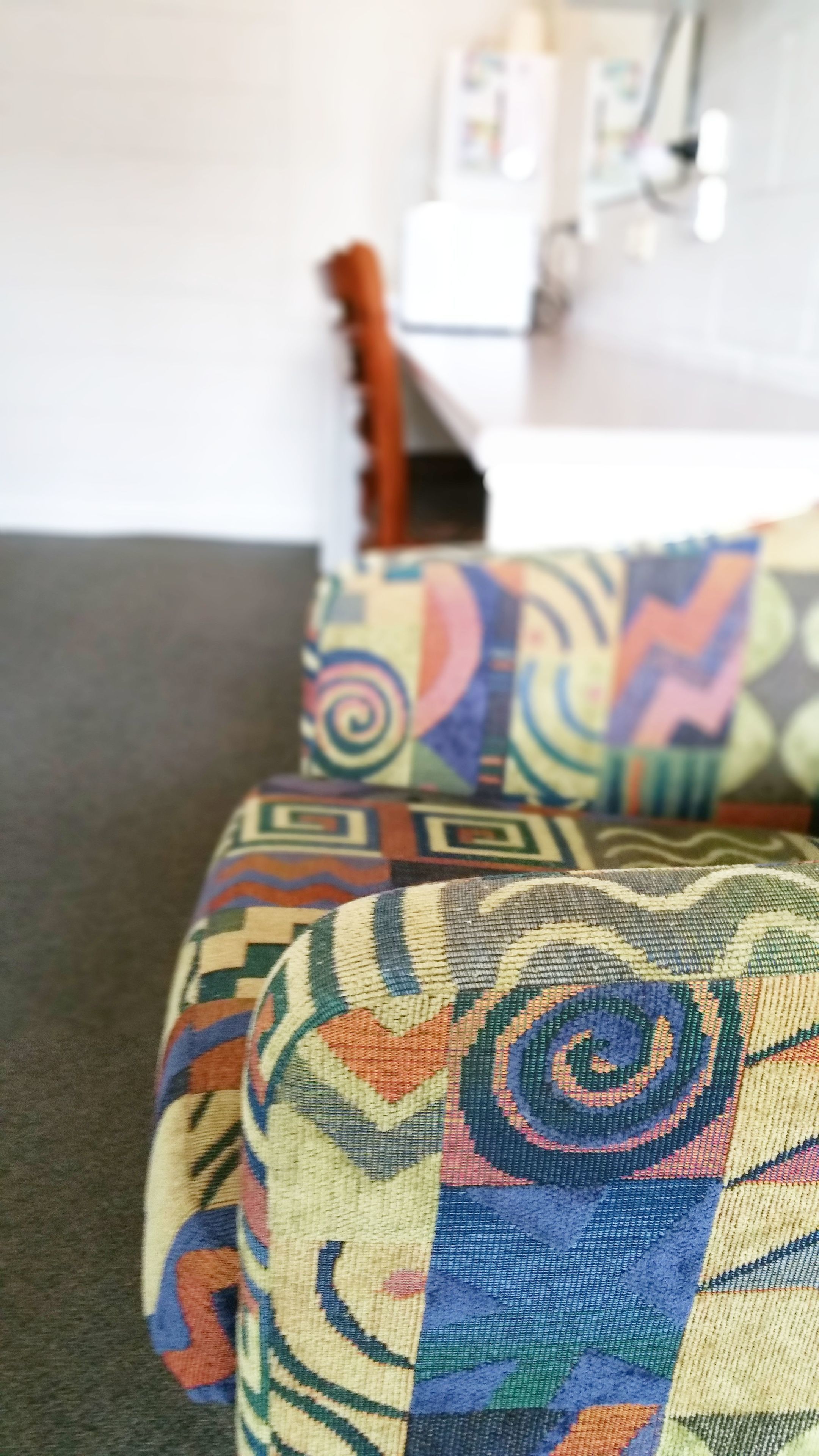 A close-up of a patterned cushion on a couch with a white wall and a door in the background.