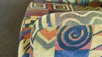 A close-up of a patterned cushion on a couch with a white wall and a door in the background.